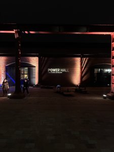 A photo taken outside the Science and Industry Museum's Power Hall: The Andrew Law Gallery. Projected onto the brick wall is a white light of text that reads: "Power Hall: The Andrew Law Gallery"
