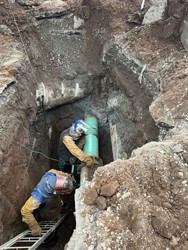 An image of a tunnel from the top. Looking down, you can see an exposed pipeline with two pipeline staff assessing the pipeline for damage