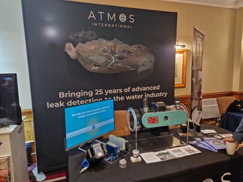 Atmos International's stand at the Global Leakage summit. There is a poster that reads the following text: "Bringing 25 years of advanced leak detection to the water industry". In front of the poster is a table containing Atmos Eclipse, a monitor and other resources.