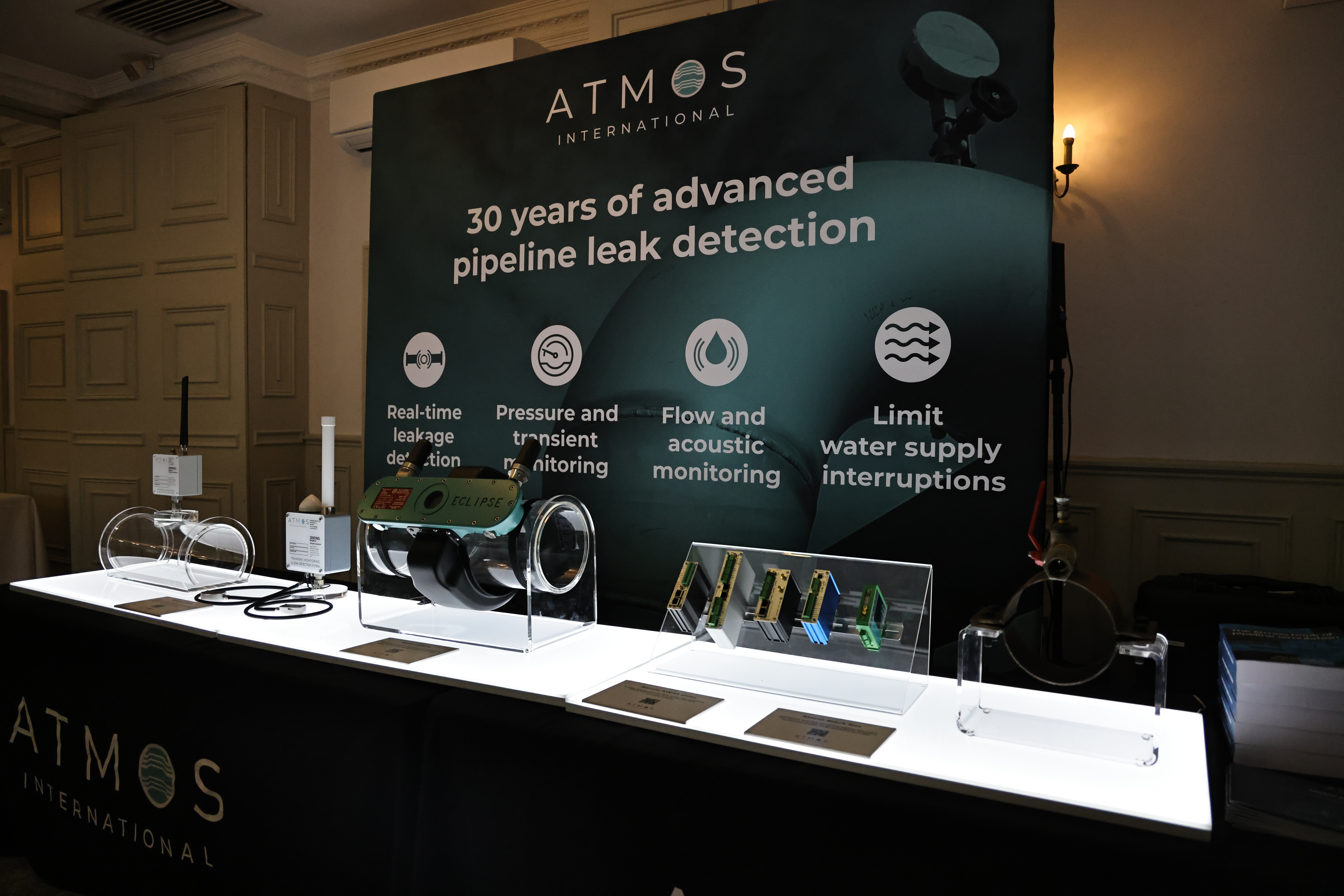 A photo containing a selection of Atmos International's water hardware in front of a sign that reads: "30 years of advanced pipeline leak detection"